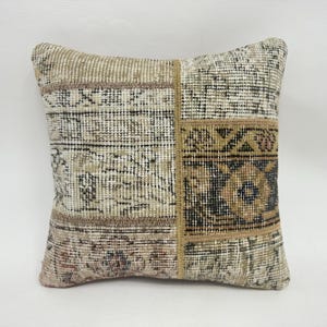 May include: Square decorative pillow with a patchwork design. The pillow features a mix of beige, brown, and olive green tones. The design includes geometric and floral patterns, creating a vintage or bohemian aesthetic.