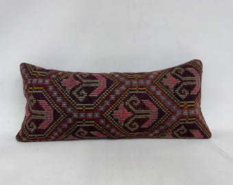 May include: A long rectangular pillow with a burgundy, pink, and yellow geometric pattern. The pillow is made of a soft, woven fabric.