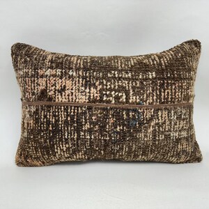 May include: Rectangular cushion with a textured, woven design. The cushion features a mix of brown, beige, and pink tones, creating a rustic aesthetic. The cushion's surface has a patchwork appearance, adding to its unique character.