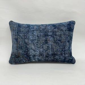 May include: A rectangular pillow with a distressed, textured appearance. The pillow features a dark blue color with lighter blue and gray accents, creating a vintage or antique aesthetic. The pillow's design suggests a woven or fabric construction.