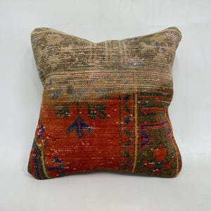 May include: A square pillow with a colorful, vintage-style rug pattern. The pillow is made of woven fabric and has a brown, orange, blue, and green color scheme.