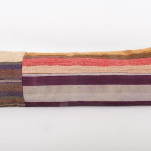 May include: Rectangular decorative pillow with a patchwork design. The pillow features a variety of colors, including beige, brown, red, and purple stripes. The pillow is made of a woven fabric and is likely used for home decor.
