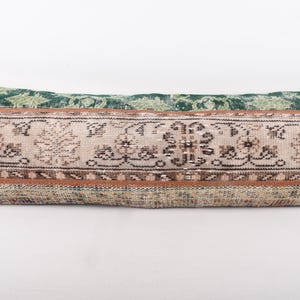 May include: Rectangular decorative pillow with a vintage rug design. The pillow features a central panel with floral and geometric patterns in beige, brown, and black, framed by a brown border. The top and bottom are green.