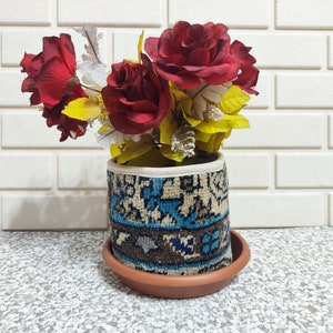 May include: A red and yellow flower arrangement in a white and blue patterned planter with a brown saucer.