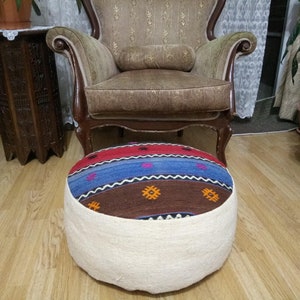 May include: A round, multi-colored patterned ottoman with a white fabric covering the bottom half. The ottoman is sitting on a wooden floor.