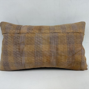 May include: A brown and beige patterned throw pillow with a subtle plaid design. The pillow is made of a soft, woven fabric and has a simple, rectangular shape.