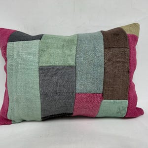 Op de afbeelding: Een patchwork kussen met verschillende kleuren en texturen, waaronder roze, groen, bruin en grijs. Het kussen is gemaakt van stofresten die in een geometrisch patroon aan elkaar zijn genaaid.