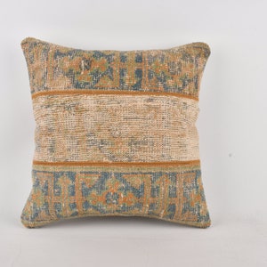 May include: A square throw pillow with a beige background and a blue and orange geometric pattern. The pillow has a fringe border.