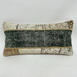 May include: Rectangular decorative pillow with a patchwork design. The pillow features a central dark green stripe bordered by tan and beige sections. The patchwork design includes various patterns and colors.