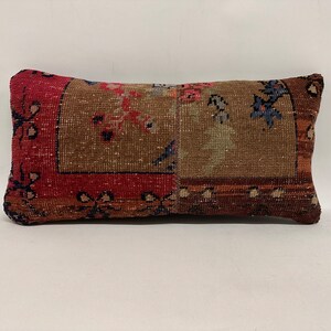 May include: Rectangular decorative cushion with a vintage rug design. The cushion features a central brown section with floral patterns, framed by a red border with dark blue accents. The cushion is approximately 50 cm long.
