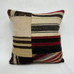May include: A patchwork pillow cover with a striped design in shades of brown, beige, red, and gray. The pillow cover is made of woven fabric and has a rustic, vintage look.