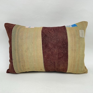 May include: Rectangular pillow with a patchwork design. The pillow features a central burgundy stripe flanked by beige and light green stripes. The ends are burgundy. Small patches of blue, pink, and white are visible.