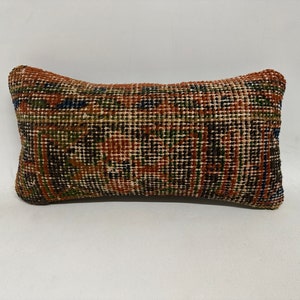 May include: A small, rectangular pillow with a brown, green, and blue patterned fabric. The pillow is made of a woven material and has a slightly textured surface.