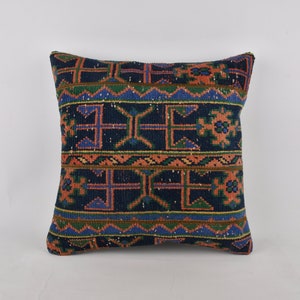 Puede incluir: Una almohada cuadrada con fondo azul y un patrón geométrico colorido. El patrón presenta colores naranja, verde y azul.