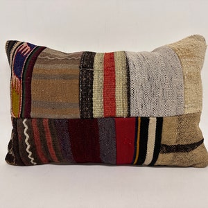 May include: A patchwork pillow with a variety of colors and patterns, including red, brown, white, and black. The pillow is made of woven fabric and has a rectangular shape.