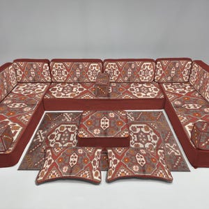 May include: A modular sectional sofa set with a patterned design in shades of red, brown, and cream. The set includes a large sofa, a rug, and several cushions. The sofa has a low profile and a modern aesthetic.