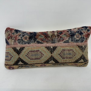 May include: A rectangular cushion with a colourful patterned fabric. The cushion has a geometric design with shades of pink, blue, green, and brown.