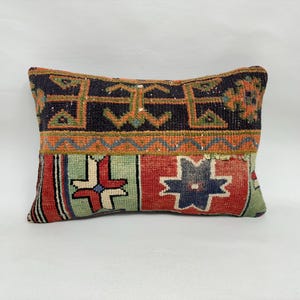 May include: Rectangular decorative pillow with a woven design. The pillow features a dark blue top section with orange and green geometric patterns. The middle section is orange, and the bottom section has red, green, and blue geometric shapes.