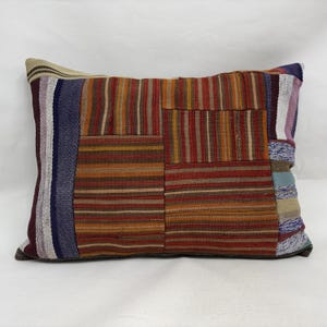 May include: Rectangular decorative pillow with a patchwork design. The pillow features a mix of warm colors, including red, orange, and brown, with striped and textured patterns. The pillow measures approximately 20 inches long and 12 inches wide.