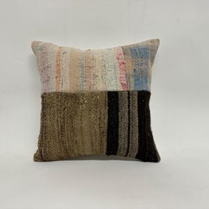 May include: A square patchwork pillow with a brown, beige, and white striped pattern on one side and a light blue, pink, and white striped pattern on the other side.