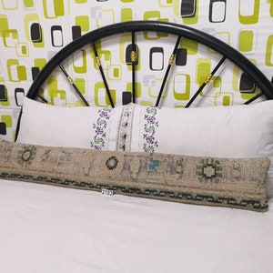 May include: A beige and green patterned bolster pillow with a white pillow behind it on a bed with a black metal headboard. The headboard has a geometric pattern of green and black squares on a white background. The pillow has the number 2182 printed on it.