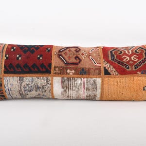 May include: Rectangular patchwork pillow with a variety of patterned fabric squares in shades of red, orange, beige, and blue. The pillow is a long, bolster style, perfect for a sofa or bed. The pillow measures approximately 30 inches in length.