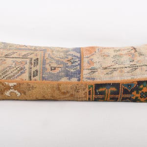 May include: A long, rectangular pillow with a patchwork design. The pillow features various sections of patterned fabric in beige, blue, orange, and brown. The pillow is a decorative item for a bed or sofa.