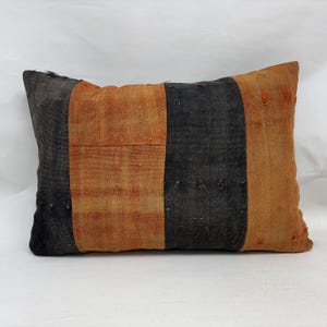 May include: Rectangular pillow with a striped design. The pillow features alternating vertical stripes of black and orange. The orange stripes have a textured appearance. The pillow is likely made of woven fabric.