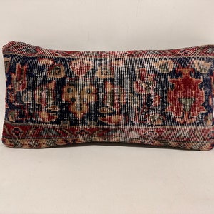 May include: A rectangular pillow with a colorful, intricate pattern. The pillow is made of a woven fabric with a red, blue, and cream color scheme. The pattern is reminiscent of a traditional rug.