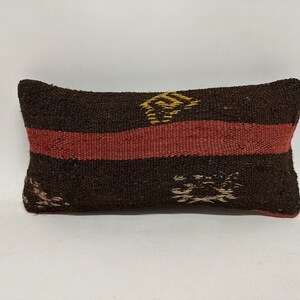 May include: A brown and red patterned cushion with a woven texture. The cushion has a rectangular shape and is filled with a soft material.