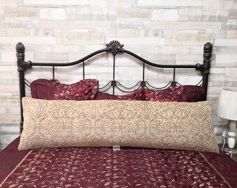 May include: A beige and brown patterned lumbar pillow with a burgundy and gold embroidered bedspread and a black metal headboard.