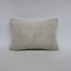 May include: A white throw pillow with a subtle woven texture. The pillow is rectangular and has a simple, minimalist design.