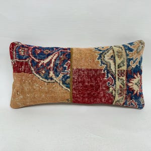 May include: Rectangular decorative pillow with a patchwork design. The pillow features sections of red, blue, and tan colors with intricate patterns. The pillow has a vintage, distressed look, suggesting it may be made from repurposed materials.