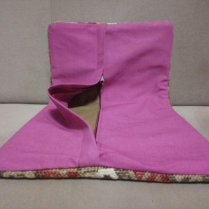 以下が含まれることがあります： ジッパー留めのピンクの布製のクッション。クッションは、茶色、白、赤のアクセントのある模様の布地で作られています。
