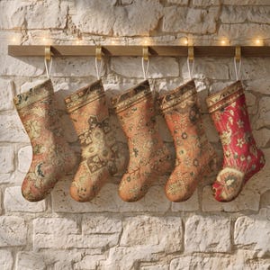 May include: Five Christmas stockings hanging from a wooden rail with gold hooks. Each stocking features a distinct, intricate woven pattern in shades of red, orange, brown, and cream, resembling traditional rug designs with floral and geometric motifs.