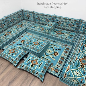 May include: A modular floor cushion set in shades of turquoise, featuring geometric patterns in orange, brown, and white. The set includes cushions, a rug, and a square ottoman, creating a cozy seating area. The text "handmade floor cushion" is visible.