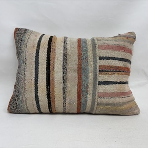 Op de afbeelding: Rechthoekig kussen met een gestreept patroon in neutrale tinten. Het kussen heeft verticale strepen in tinten beige, zwart, bruin en rood. Het kussen is gemaakt van een geweven stof, waardoor het een textuur heeft.