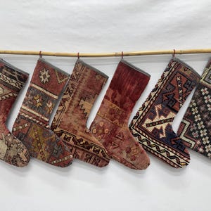 May include: Six Christmas stockings hanging in a row on a bamboo rod. Each stocking features a unique, intricate woven pattern with varied color palettes including shades of red, brown, blue, cream, and black, finished with a grey fabric trim.
