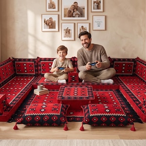 May include: A U-shaped floor seating arrangement featuring red and black patterned cushions with tassels. The set includes a central rectangular table, backrest cushions, and floor pillows, all decorated with geometric motifs and borders.