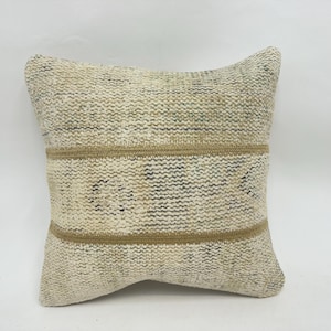 May include: Square decorative pillow with a textured, off-white background and two horizontal tan stripes. The pillow has a woven appearance with subtle variations in color, adding to its rustic charm. The pillow is a square shape.