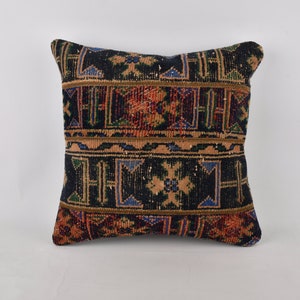 May include: A square throw pillow with a black background and a colorful geometric pattern. The pattern features shades of red, orange, blue, and green.