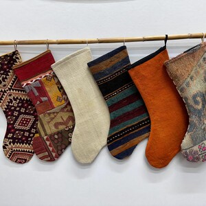 May include: Six colorful Christmas stockings made from repurposed fabric. The stockings are hung on a wooden rod and feature a variety of patterns and colors, including red, blue, green, and white.