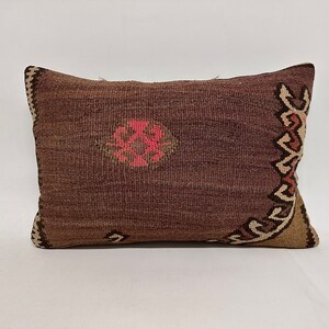 May include: A brown and beige patterned throw pillow with pink accents. The pillow is made of woven fabric and has a rectangular shape.