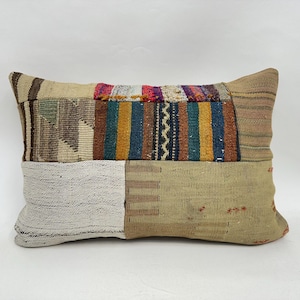 May include: Rectangular patchwork pillow with a variety of colors and textures. The pillow features sections of beige, brown, green, blue, and red fabrics. The design includes stripes, geometric patterns, and woven textures.