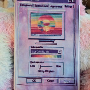 May include: A cross-stitch embroidery depicting a vintage computer display properties window in shades of purple and pink. The screen shows a sunset landscape with palm trees. Text includes Display Properties, Color palette, and 640 by 480 pixels.