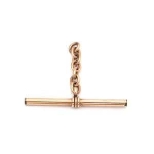 May include: A rose gold-toned watch chain T-bar component featuring a horizontal cylindrical bar with a central decorative ribbed band, connected to a short vertical segment of oval-shaped metal links extending upward from the center.