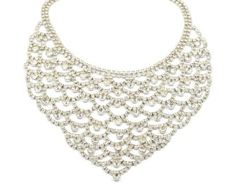 May include: A silver-toned statement necklace with a cascading, layered design. The necklace features multiple rows of small, clear rhinestones, creating a sparkling, elegant look. The necklace has a delicate chain and clasp for closure.