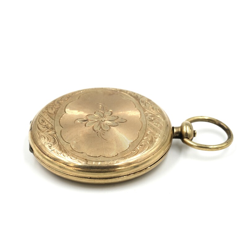 May include: A gold-colored pocket watch with an engraved floral design on the cover. The watch has a circular shape with a loop for a chain. The watch is set against a white background.