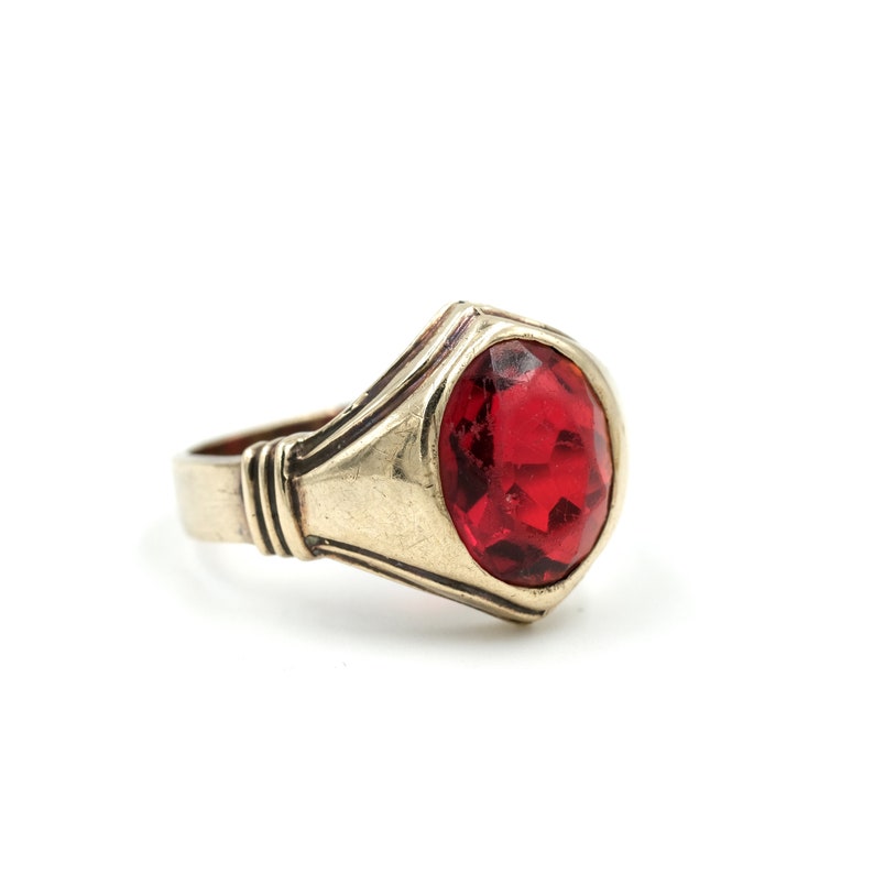 May include: A gold ring with a large, red gemstone. The ring has a simple, elegant design.