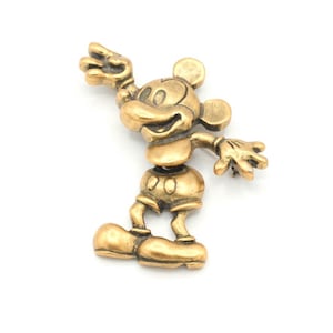 Peut inclure: Figurine dor&eacute;e de Mickey Mouse en position debout, une main lev&eacute;e et l'autre tendue. La figurine a de grandes oreilles, un short et des chaussures. Le design g&eacute;n&eacute;ral est une repr&eacute;sentation classique du personnage embl&eacute;matique.
